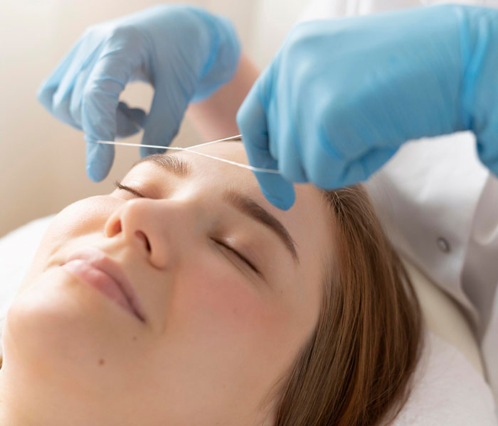 beautician shaping client's eyebrows with precision threading technique